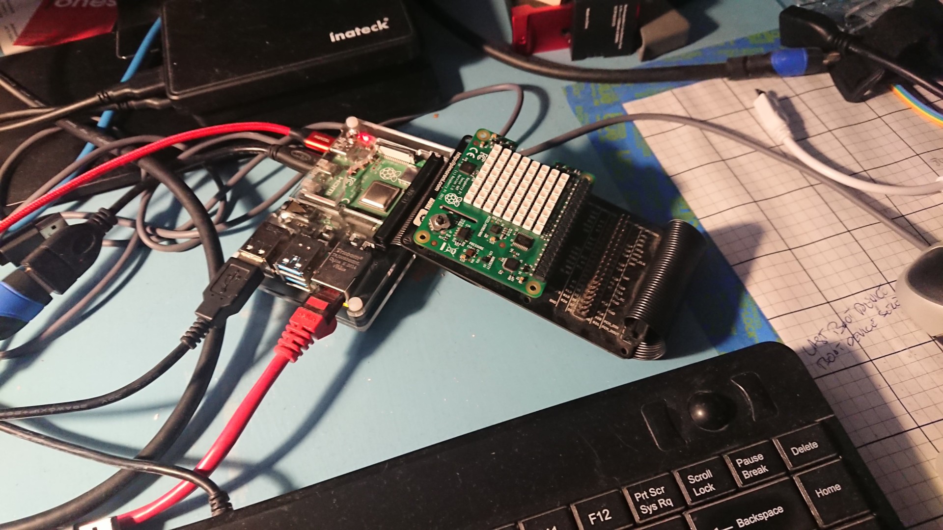 A Sense HAT installed on a Black HAT Hacker board, attached by a black ribbon cable to the GPIO header of a Pi 4B 8GB